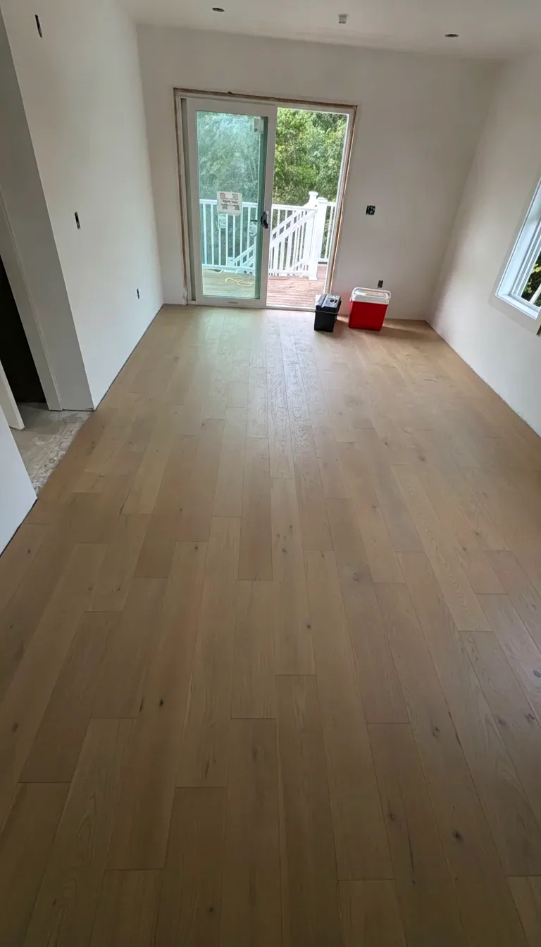 Finished white oak hardwood floor leading to a sunlit patio door